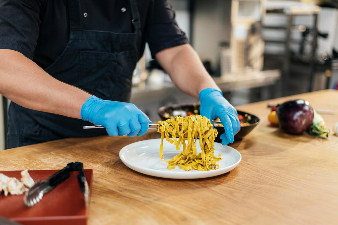 male-chef-with-gloves-putting-pasta-plate