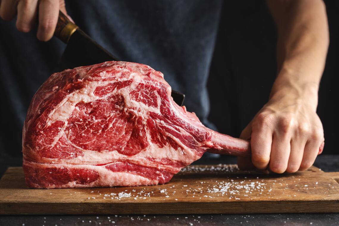 BOUCHER butcher-cuting-fresh-appetizing-tomahawk-steak-old-wooden-board-closeup-min