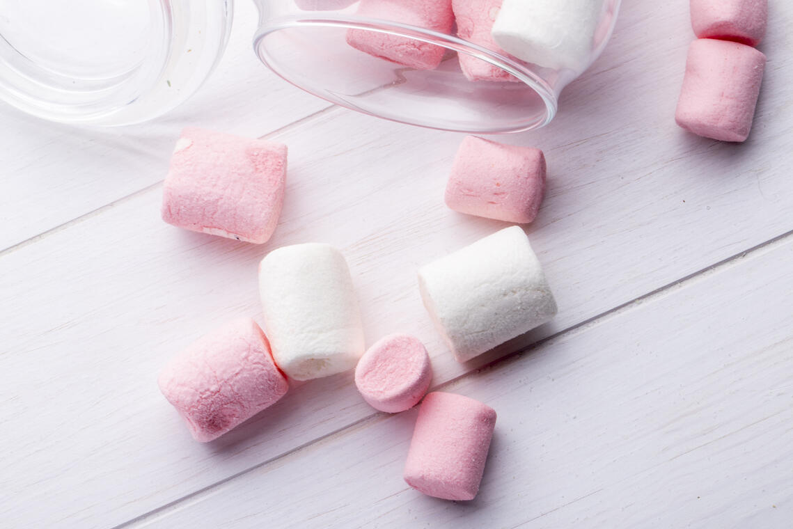 top view of colorful marshmallow scattered from a glass jar on rustic background