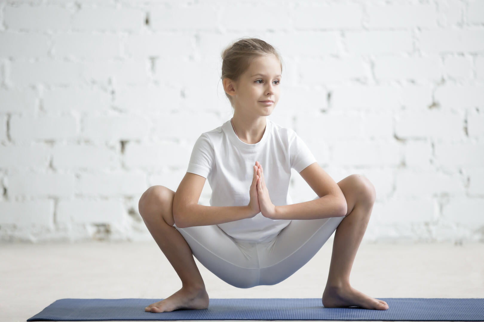 Girl child in Malasana pose, white studio background