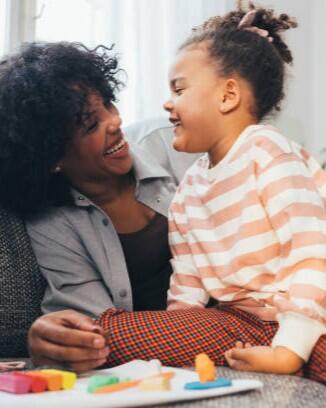 An adorable preschool child and her nanny sitting on the sofa and having fun.