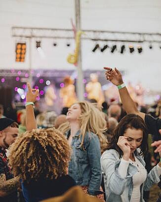 Group of friends dancing together in a marquee at an outdoor music festival.