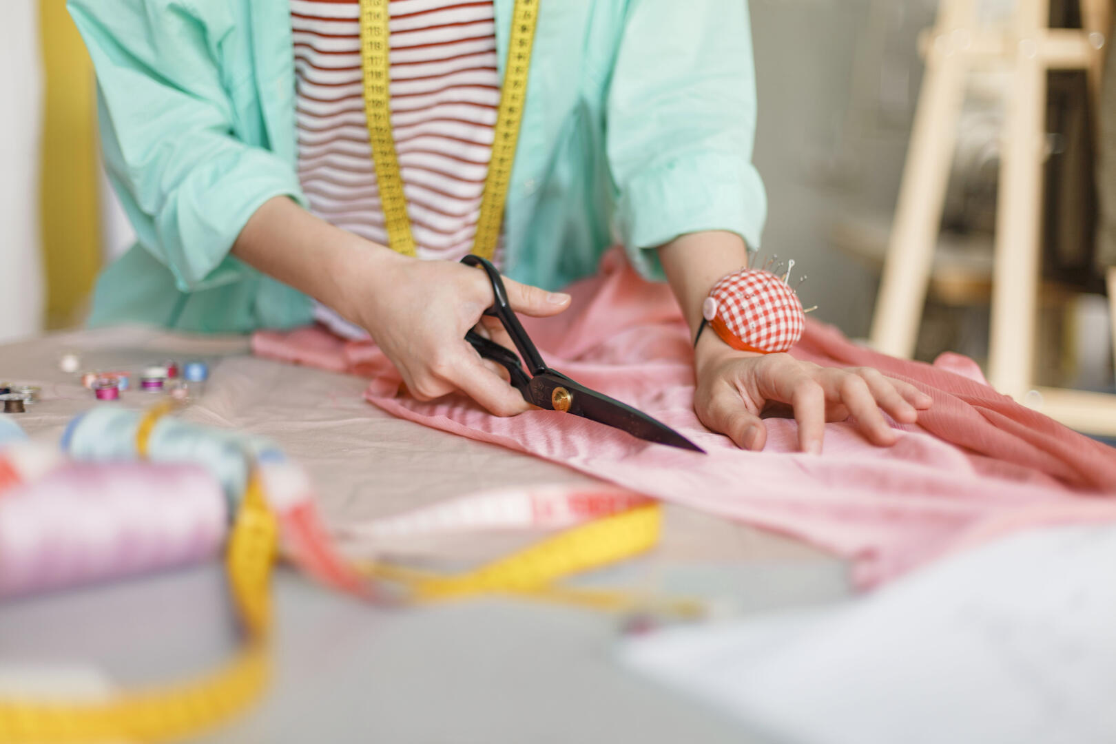 Close up seamstress cutting fabric with scissors in sewing workshop