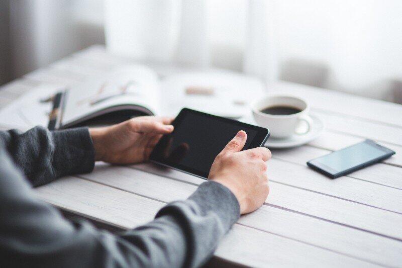 man-holding-digital-tablet-with-coffee-cup-and-mobile-phone-on-wooden-table-186675