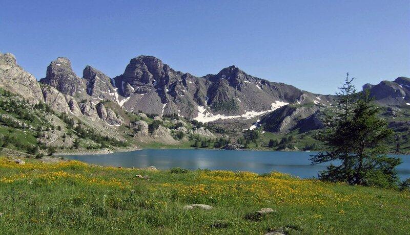 Le lac d'Allos au mois de juillet, nombreuses fleurs encore présentes et des névés résiduels au pied des Tours du lac.
