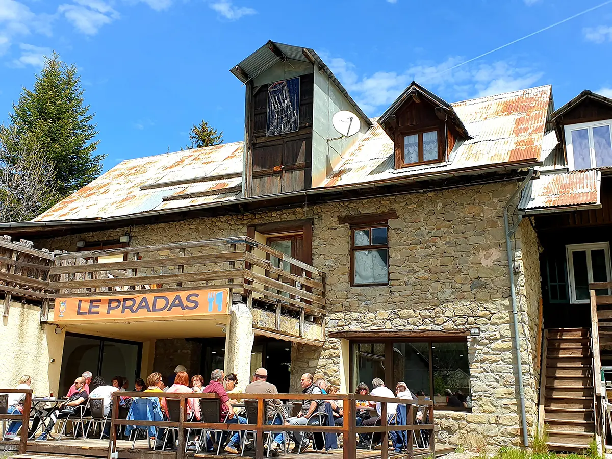 Restaurant dans une bâtisse en bois et pierre, avec terrasse en bois au RDC, tables et chaises