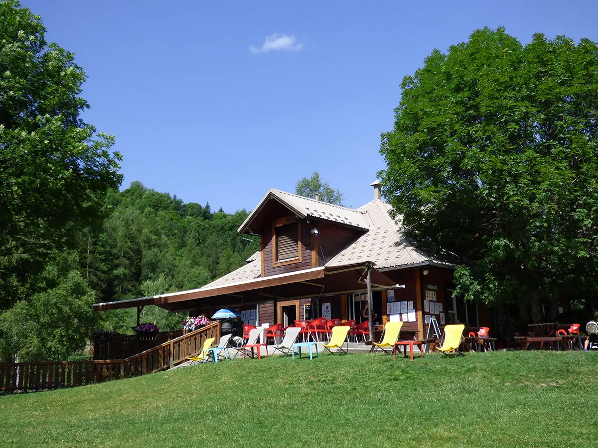 Vue d'ensemble du restaurant du Parc de Loisirs, bâtiment en bois sur 2 étages avec terrasse (tables, chaises, chaises longues), dans un cadre forestier
