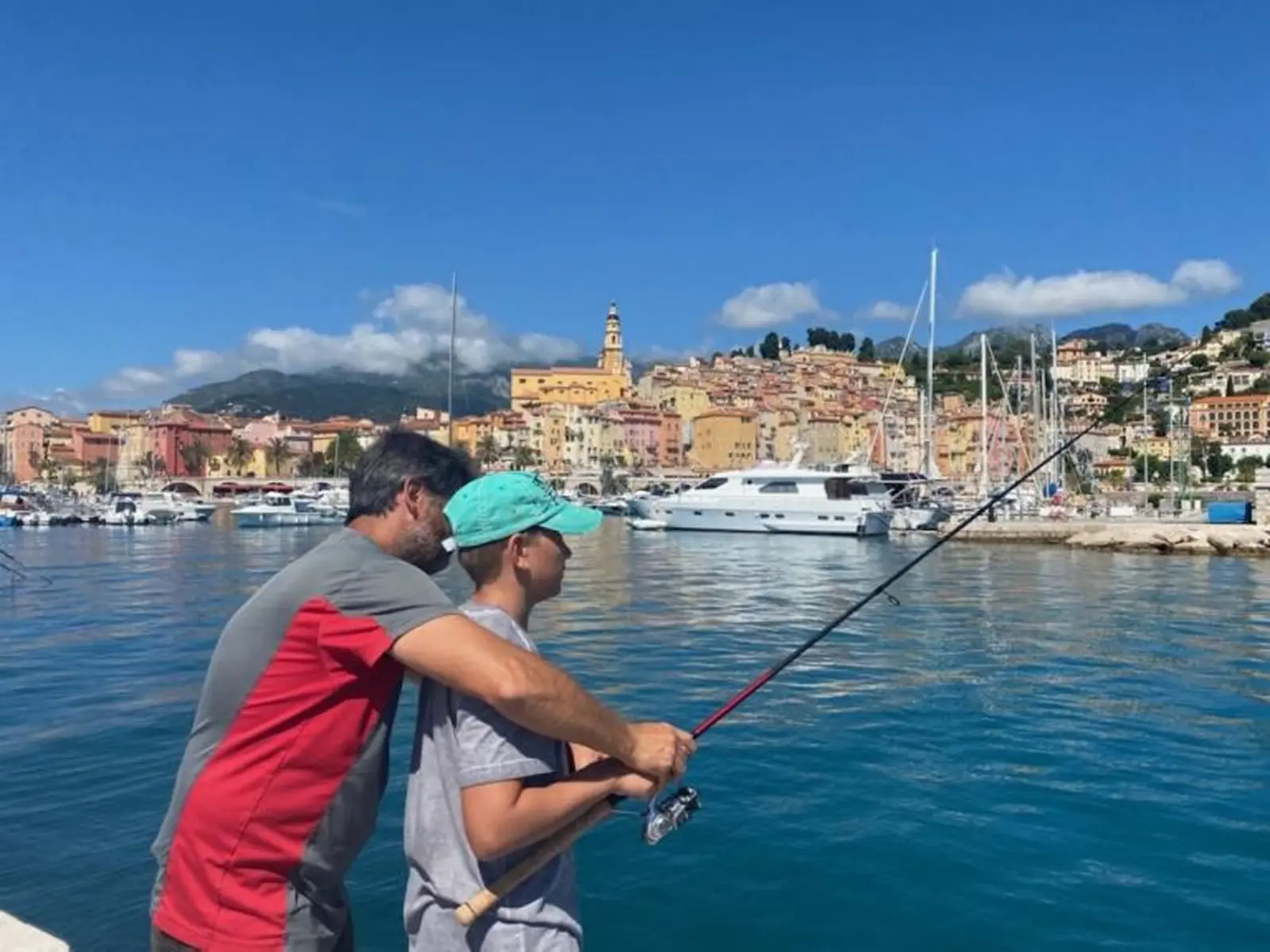 1 adulte aprenant à un jeune à pêmcher à la ligne