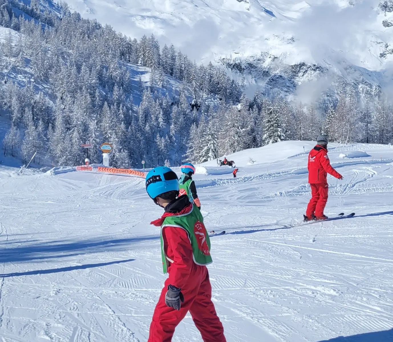 Un enfant au 1er plan qui skie, un moniteur ESF derrière