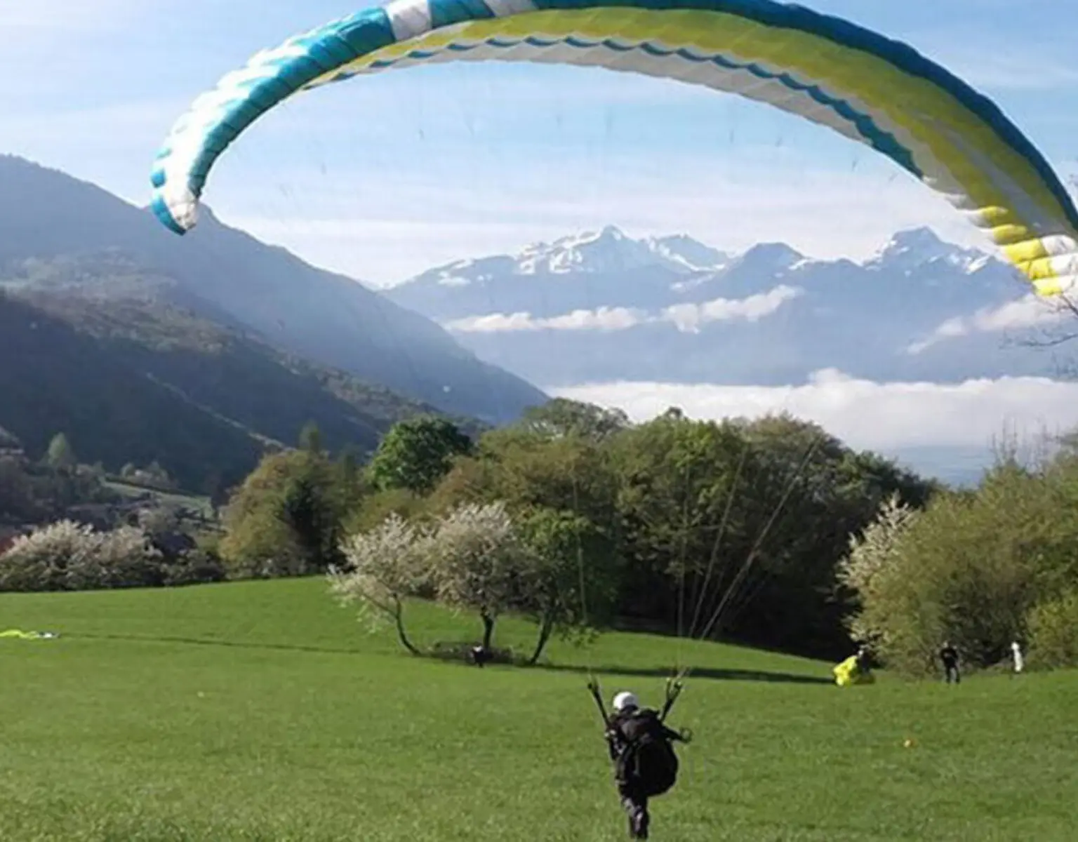 un parapente en pente école dans un grand champ vert des nuages et les montagnes en arrière plan