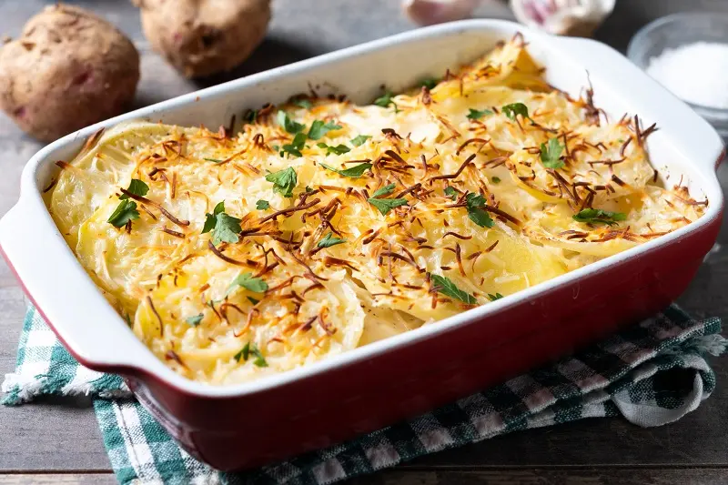 Potato gratin baked with cream and cheese on wooden table.