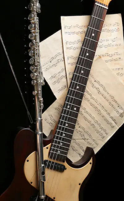 Flute, electric guitar and note sheets on black background