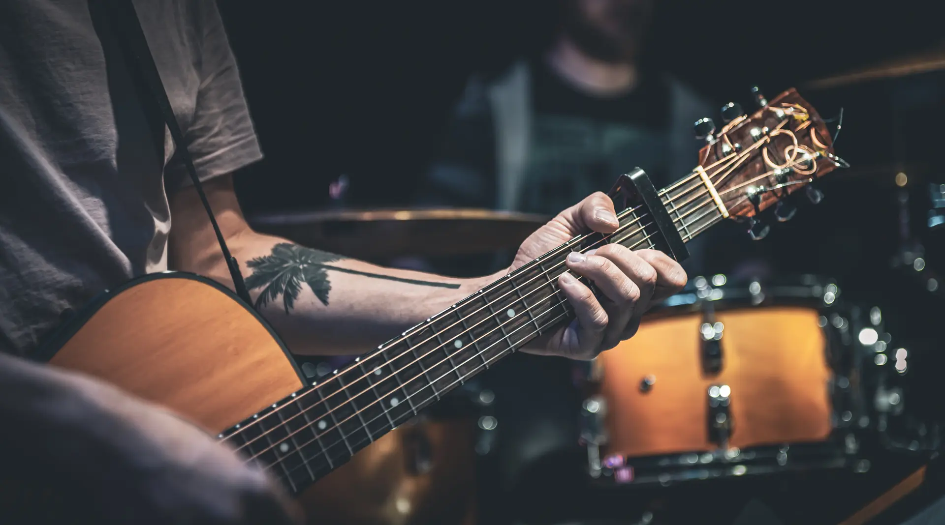 A man plays an acoustic guitar in the dark, close-up.
