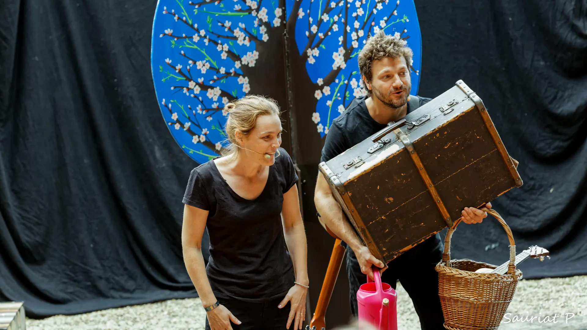 Un couple sur scène. L'homme tient une valise dans ses bras.