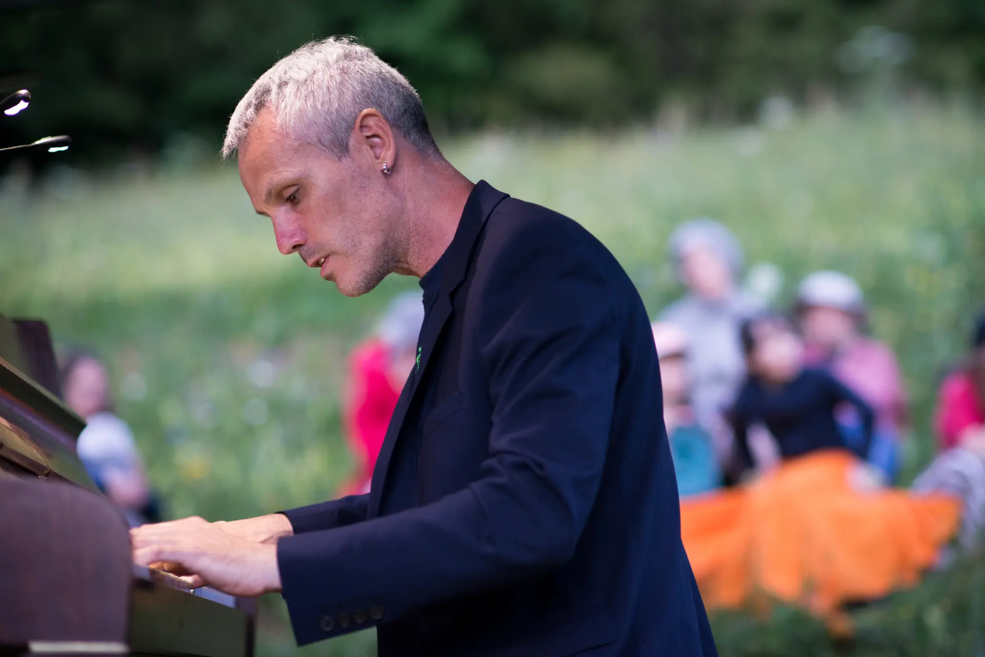 Alexandre Guhéry joue du piano droit en plein air devant un public assis dans l'herbe.