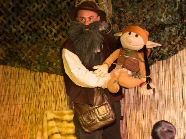 Yann, comédien, debout sur scène, déguisé en lutin avec une marionnette dans les mains.