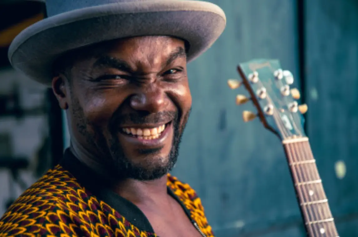 artiste avec chapeau et guitare qui sourit