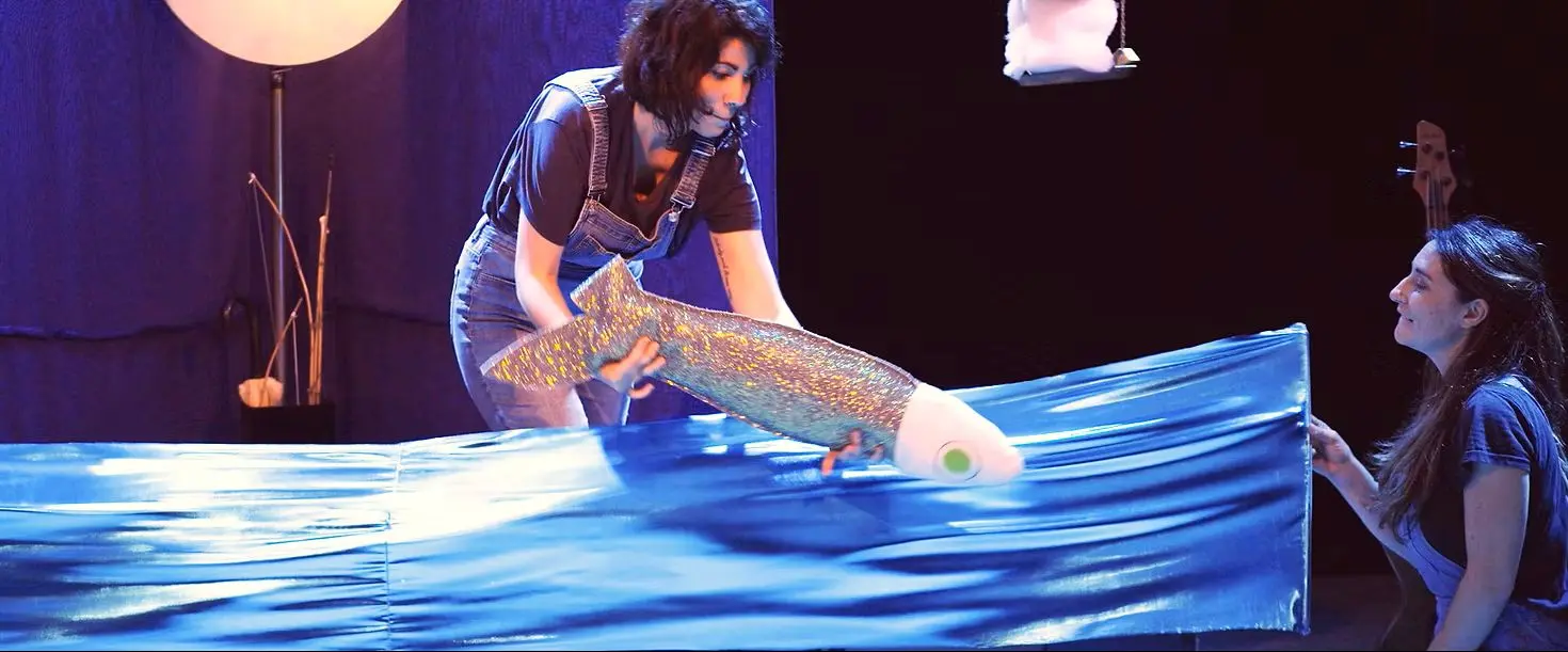 deux artistes sur scène avec une peluche en forme de poisson qui saute dans l'eau