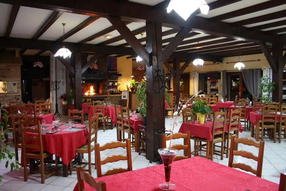 Vous vous trouvez dans une pièce spacieuse, avec un plafond haut soutenu par des poutres en bois. Des tables rondes, séparées par des chaises en bois, occupent la majeure partie de l'espace.