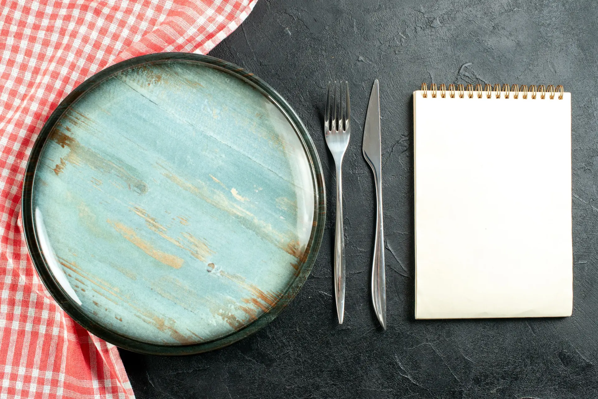 Une nappe à carreaux avec une assiette verte, une fourchette, un couteau et un bloc-notes