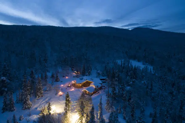 Photo d'un bâtiment ossature bois au milieu d'une forêt de sapins, de nuit, sous la neige : le restaurant du Clariant.