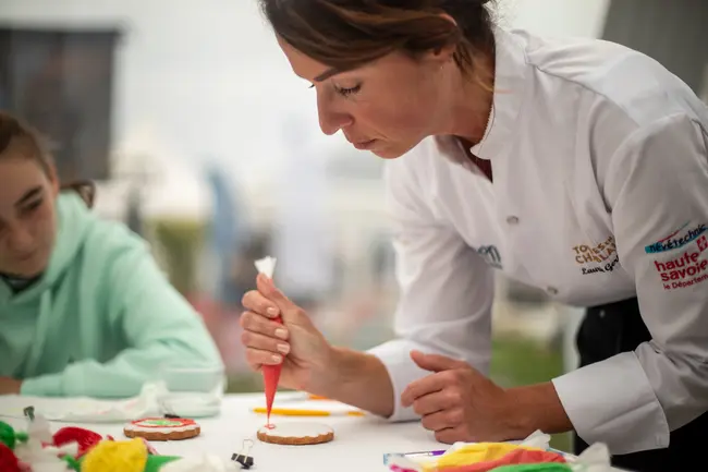 Une patissière décore un biscuit à l'aide d'une poche à douille