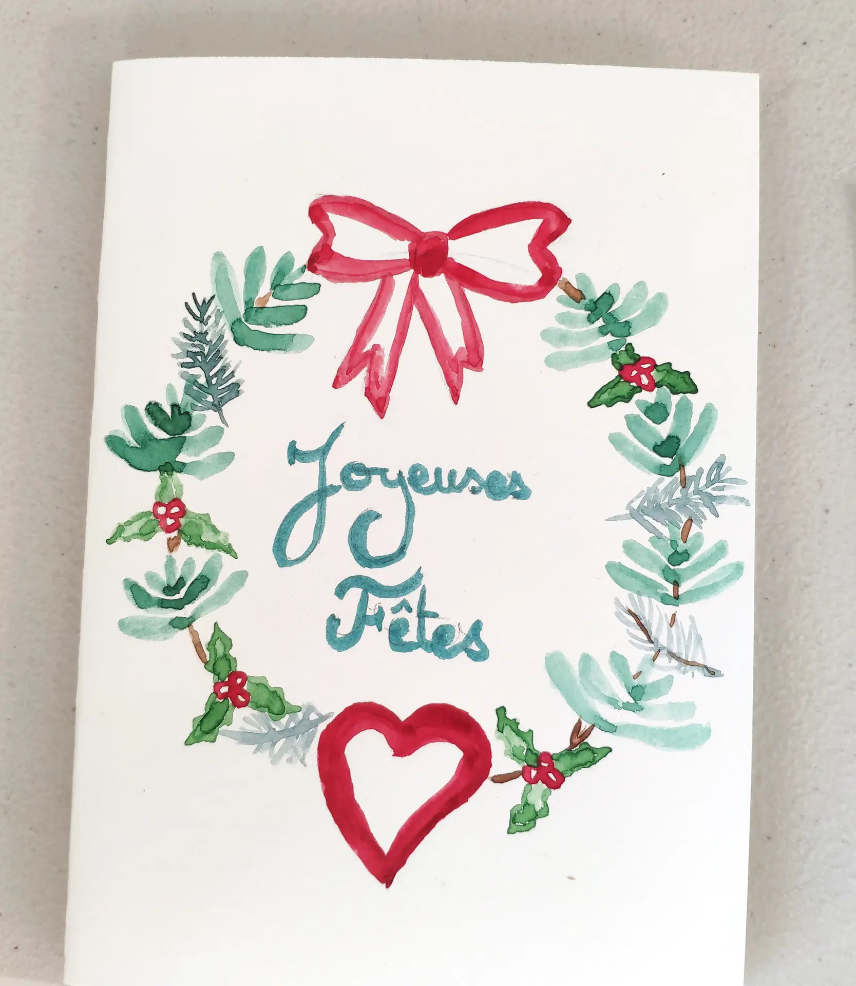 réalisation d'une carte de vœux à l'aquarelle représentant une couronne de Noël et marqué Joyeuses fêtes