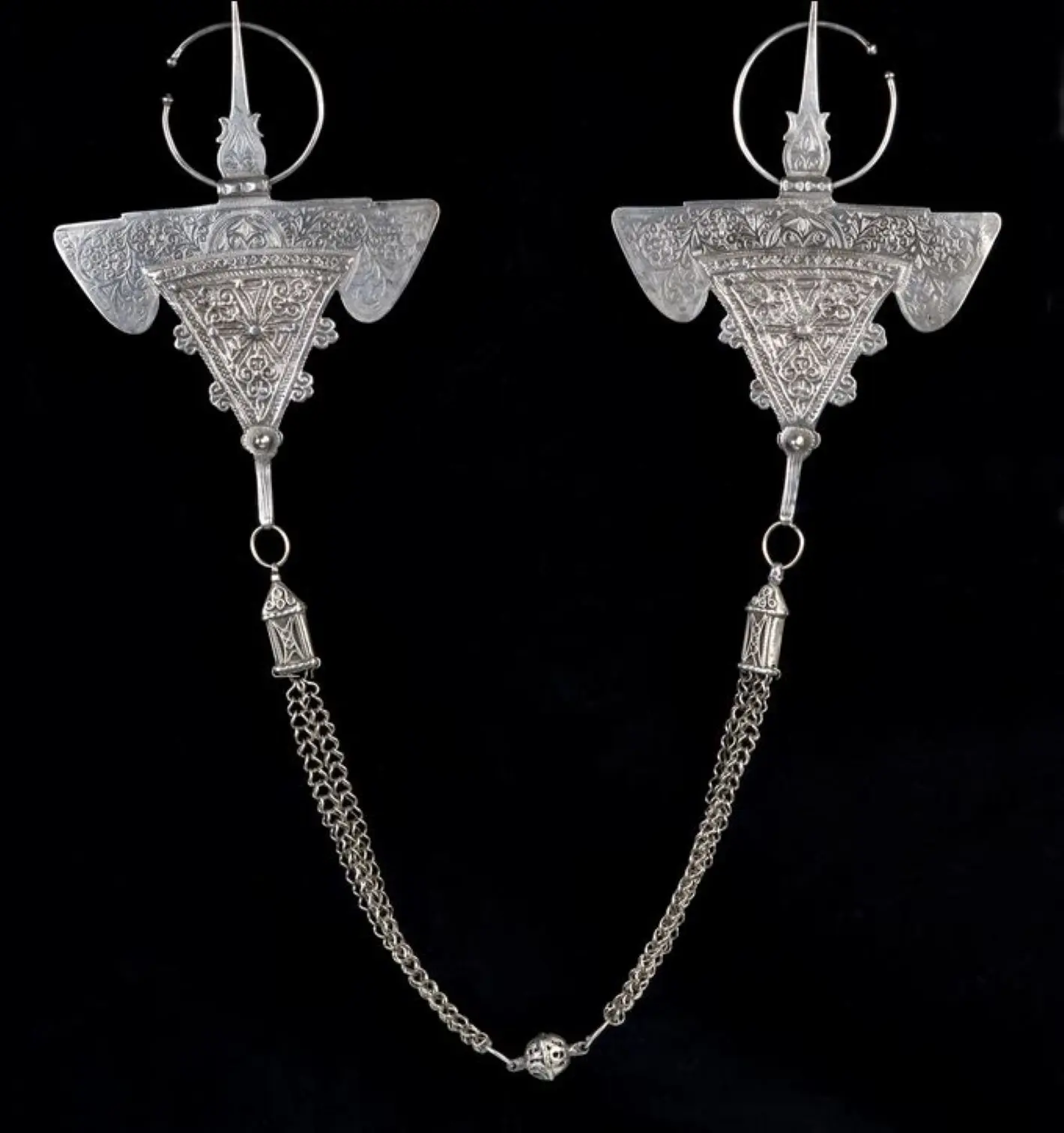 Paire de fibules [tizerzaï] et chaîne, dites fibules du « bélier ». Ilhahane, région d'Essaouira, fin 19ème - début 20ème siècle. Argent. 17 x 14 cm ; largeur totale : 103 cm. Musée Pierre Bergé des arts berbères - Fondation Jardin Majorelle