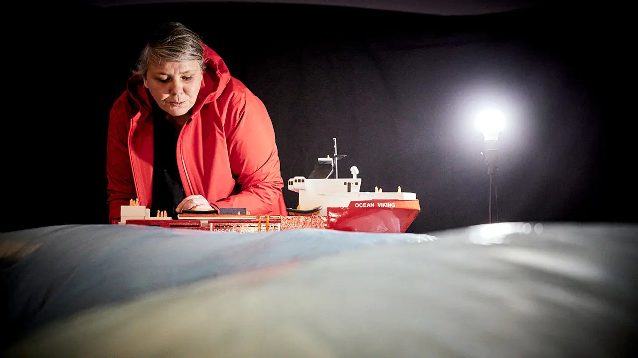 femme en doudoune rouge devant une maquette de bateau rouge