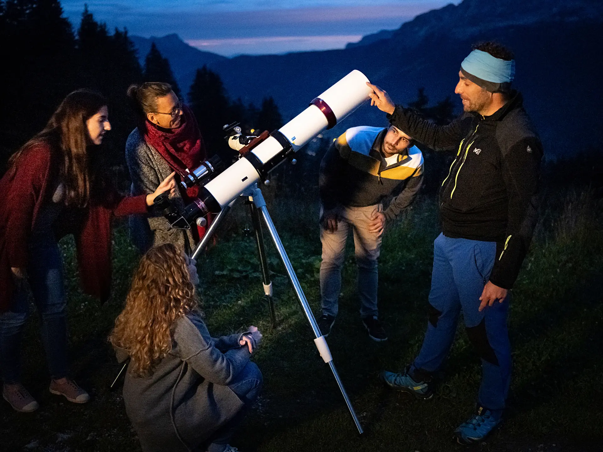 Un groupe est installé autour d’un télescope, tandis que le guide de moyenne montagne leur montre les étoiles.
