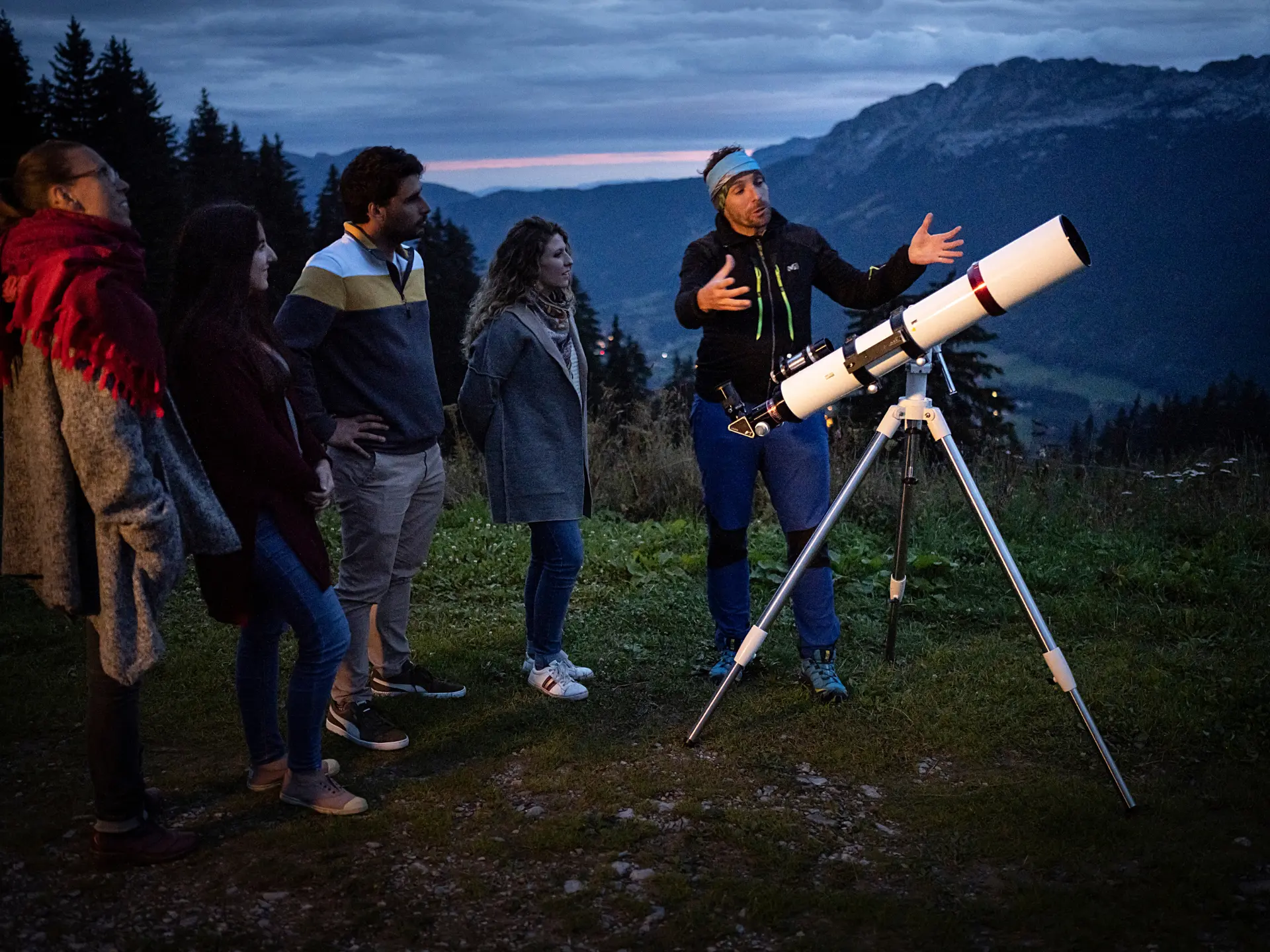 Un groupe est installé autour d’un télescope, tandis que le guide de moyenne montagne leur montre les étoiles.