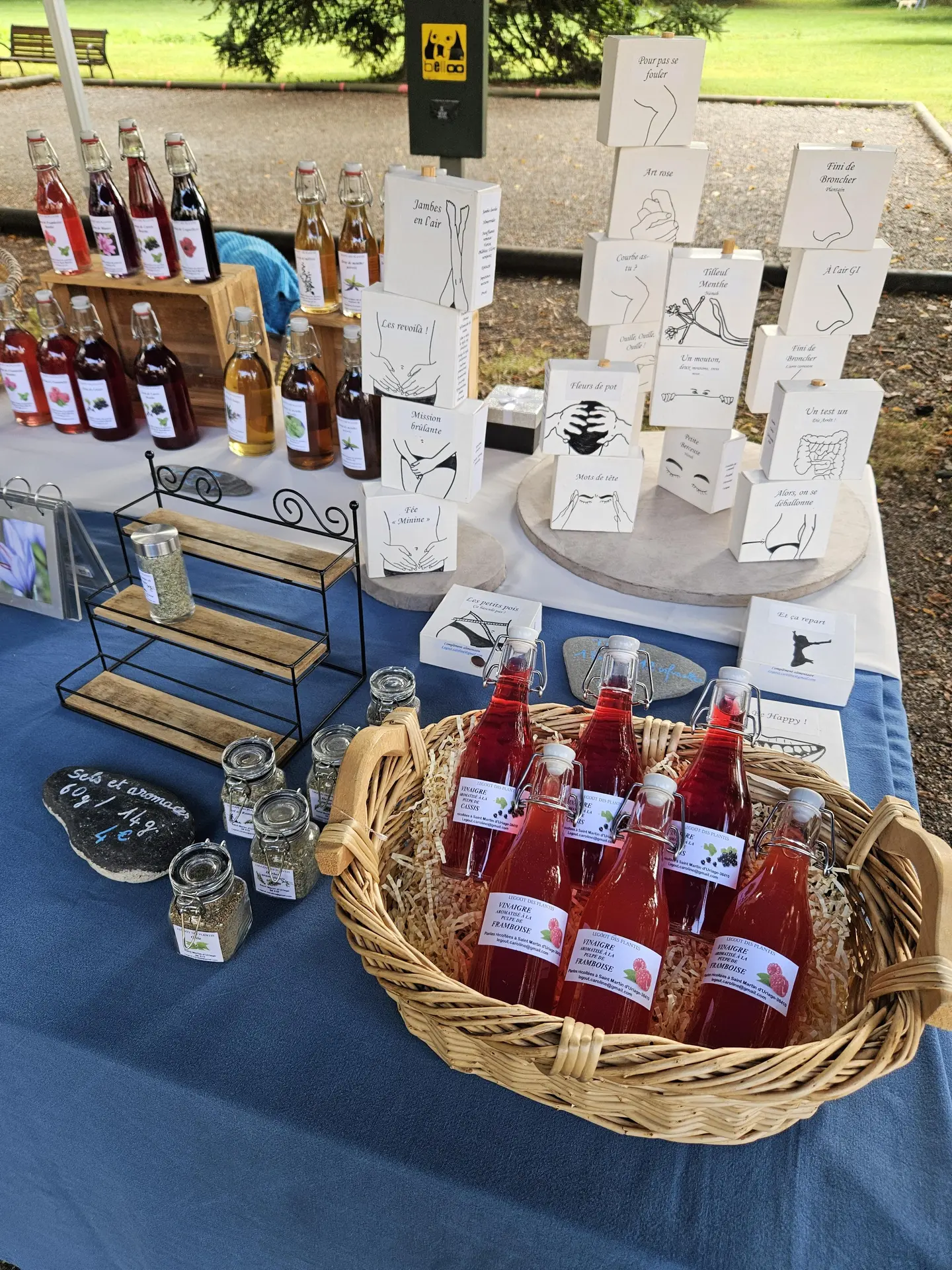 Ce stand de marché présente une variété de produits artisanaux à base de plantes : sirops, tisanes et herbes aromatiques.
