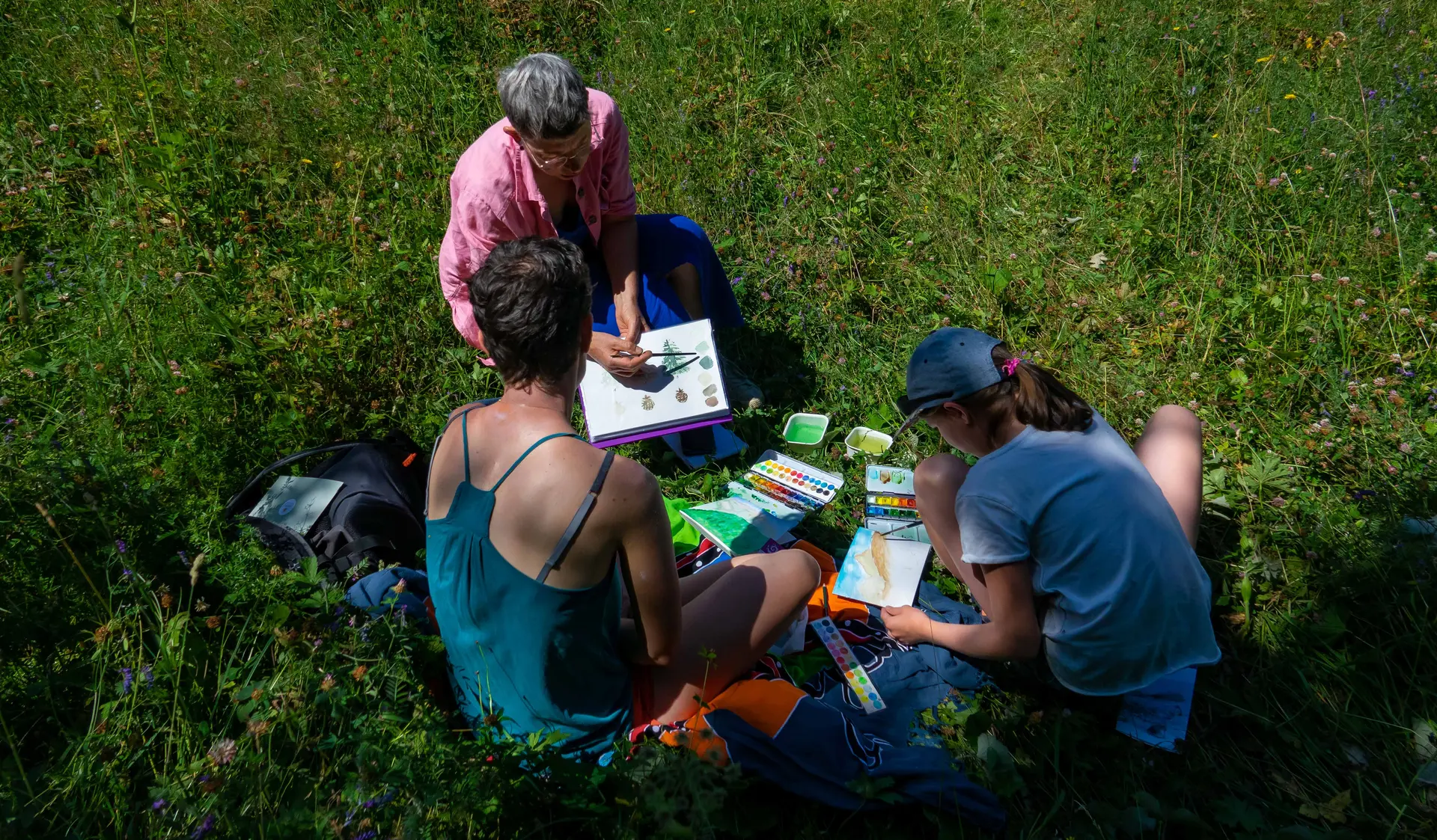 Emelyne explique les techniques de l'aquarelle à deux femmes assises dans l'herbe.