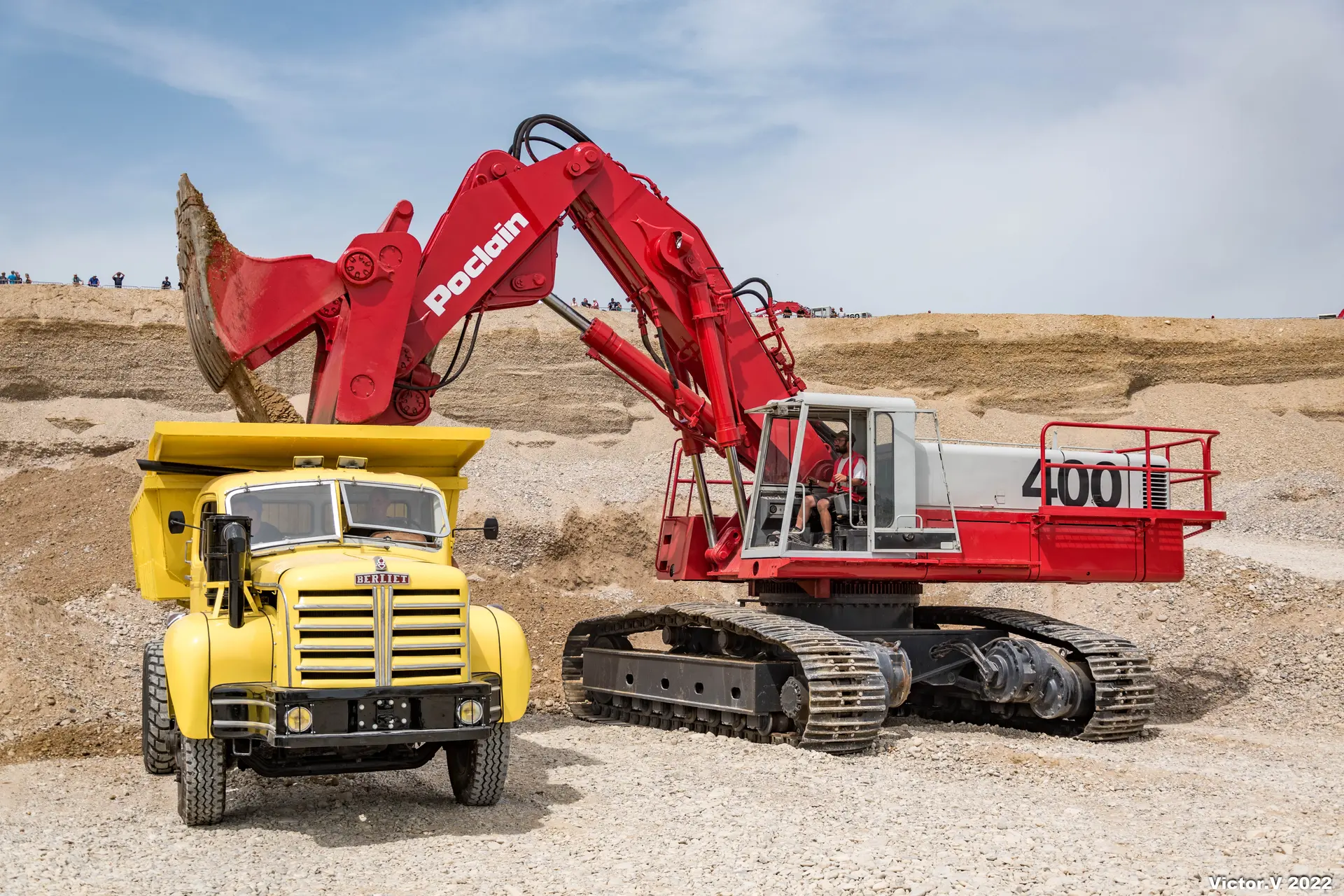 Photo montrant une pelleteuse remplissant avec son godet la benne d'un camion de sable