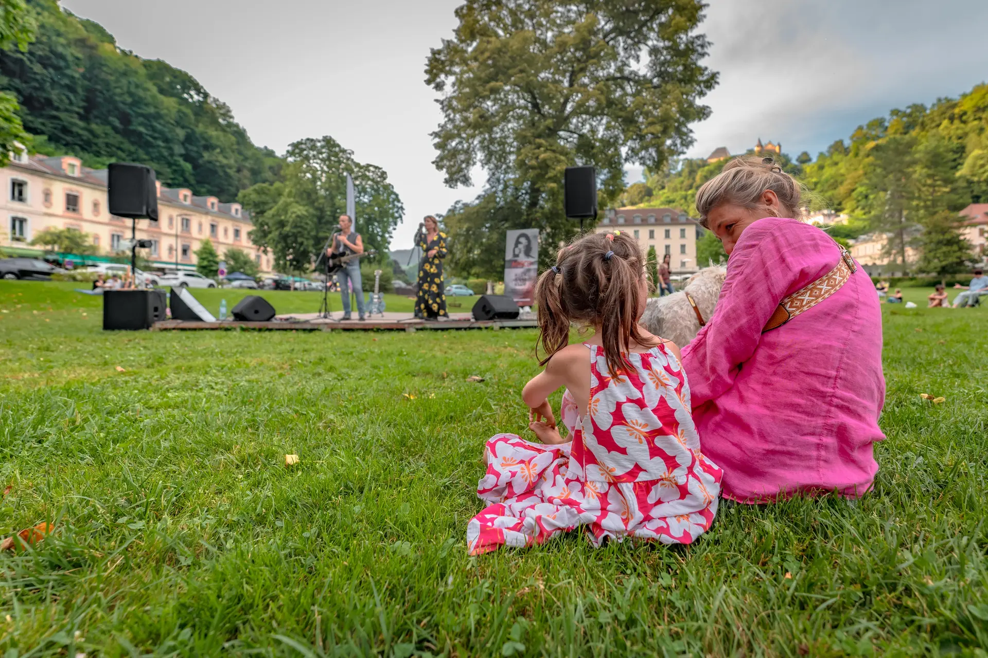 Une maman et sa fille assisent dans l'herbe durant un concert dans le parc d'Uriage.nt la foule.
