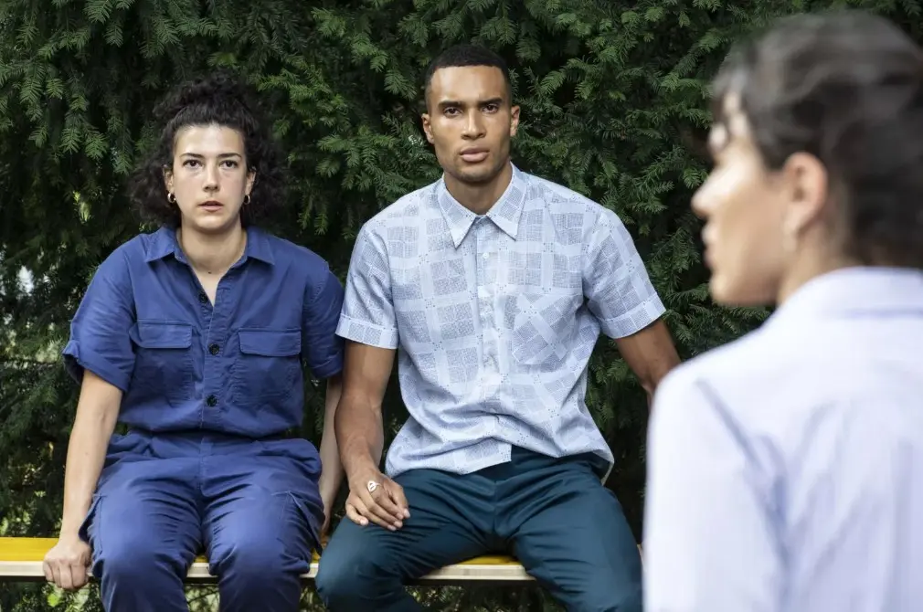 3 comédiens, un de dos au premier plan, les deux autres nous font face assis sur un banc