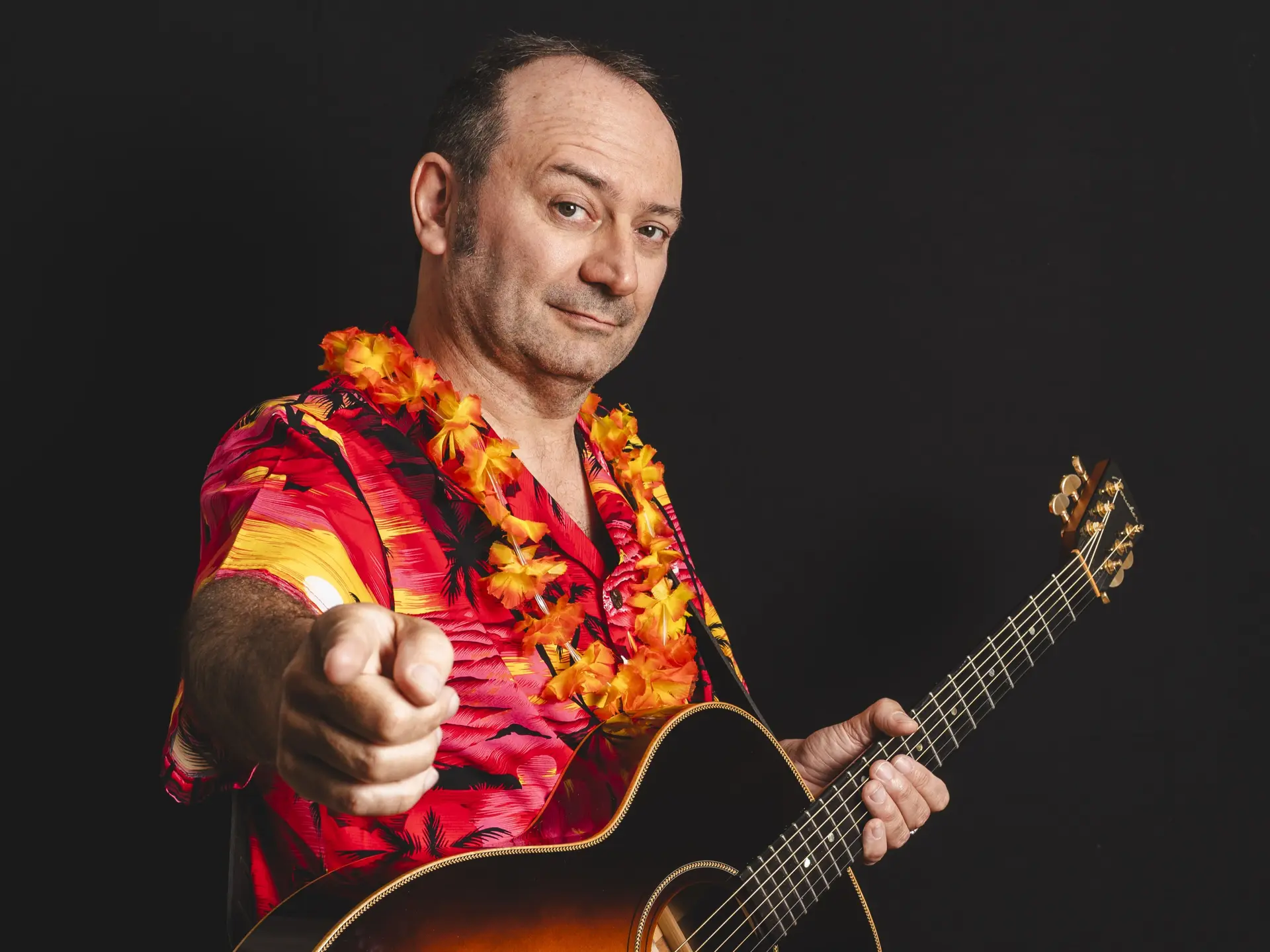Un homme avec une chemise hawaïenne, un collier de fleurs et une guitare.