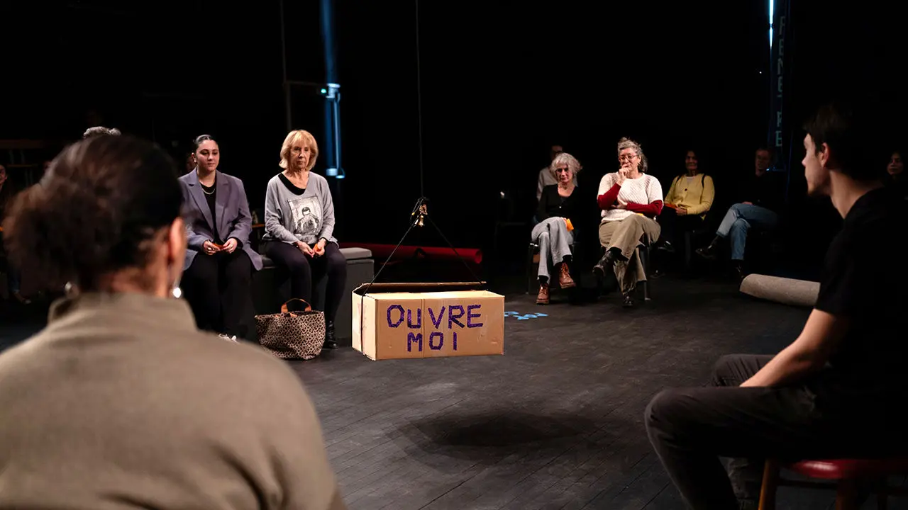 personnes sur scène assises autour d'un carton qui dit ouvrez moi