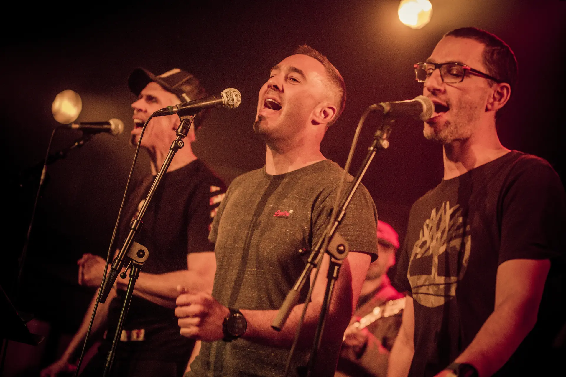 Un trio d'hommes chantant dans des micros sur pied.