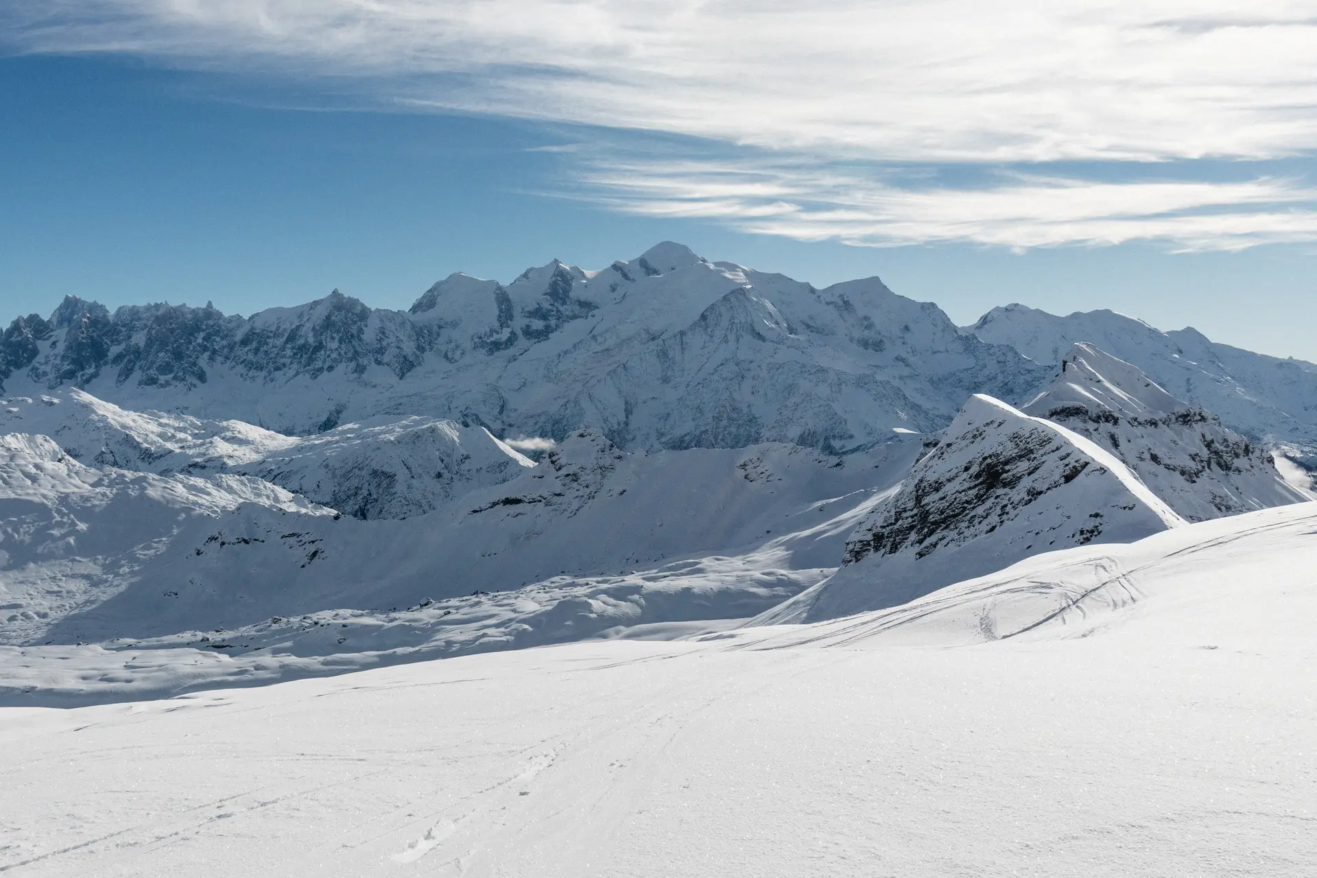 Le sommet enneigé du Mont-Blanc domine l'horizon au centre d'un vaste panorama alpin sous un ciel bleu clair.