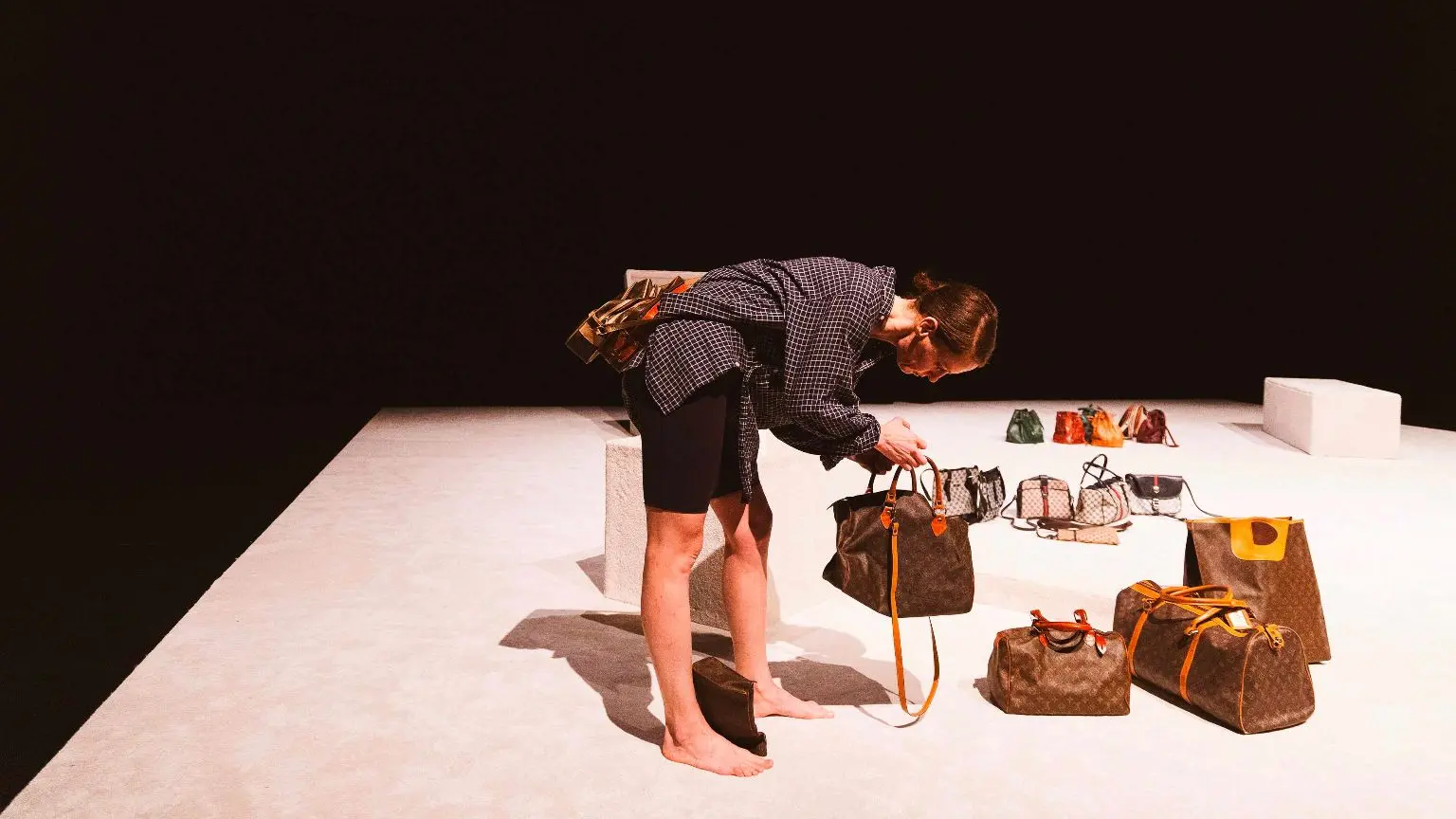 femme sur scène entourée de nombreux sacs posés au sol