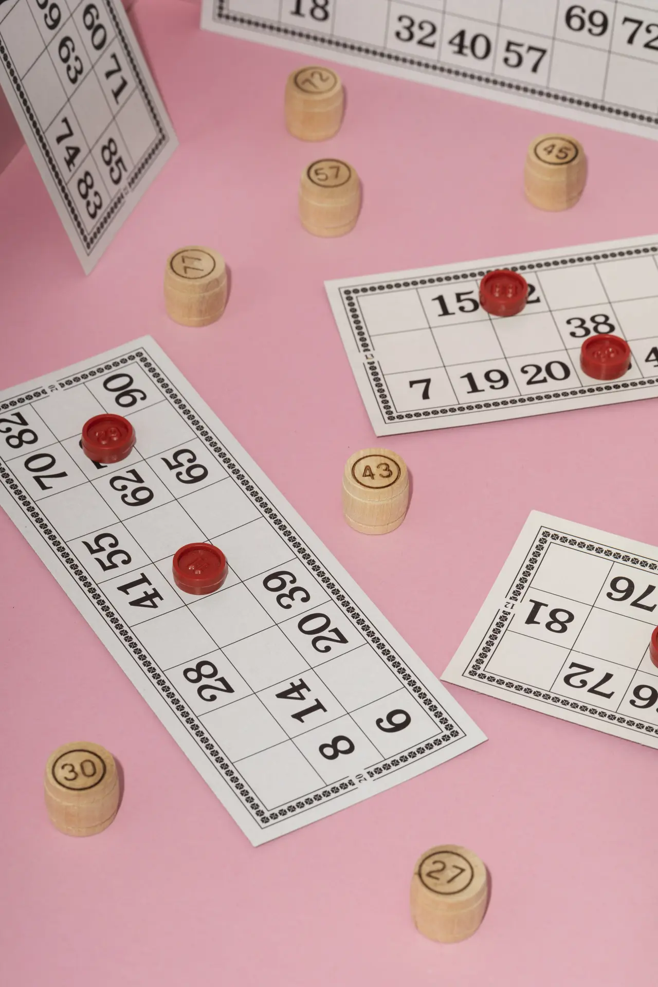 Des cartons et des jetons de Loto sont posés sur un fond rose bonbon.