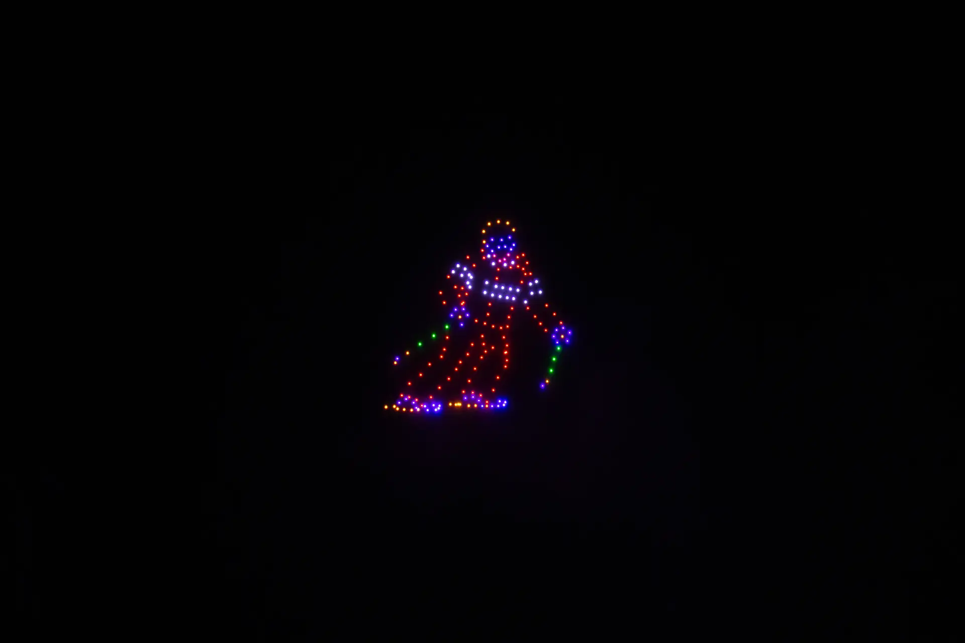 Dans un ciel nocturne totalement noir, des centaines de drones lumineux forment la silhouette colorée d’un skieur en plein virage