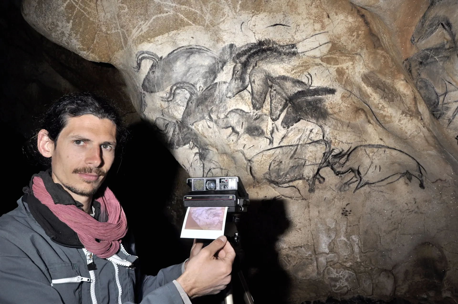 un homme prend une photo d'une peinture murale dans une grotte