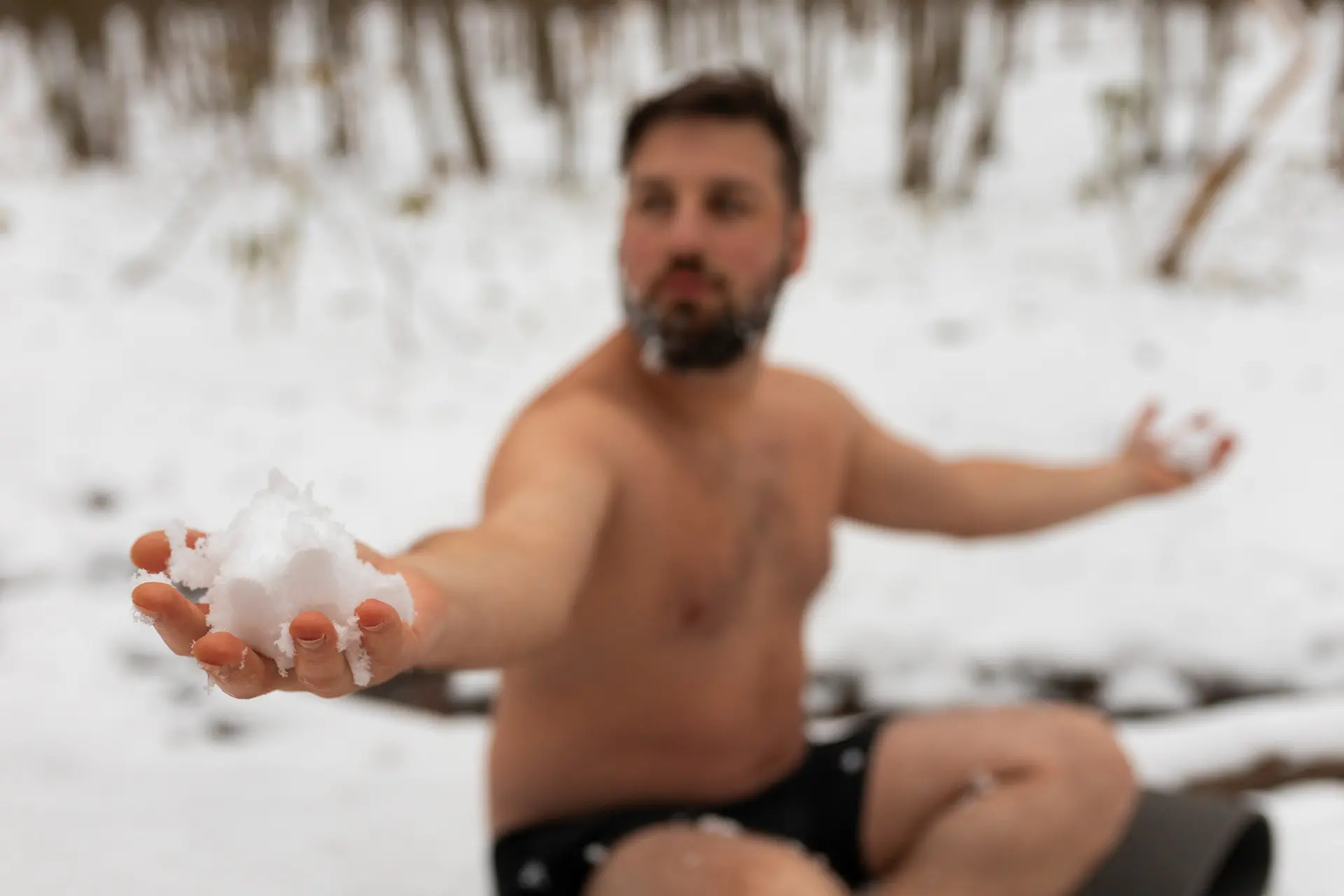Homme tenant une boule de neige tout en étant assis par terre en slip