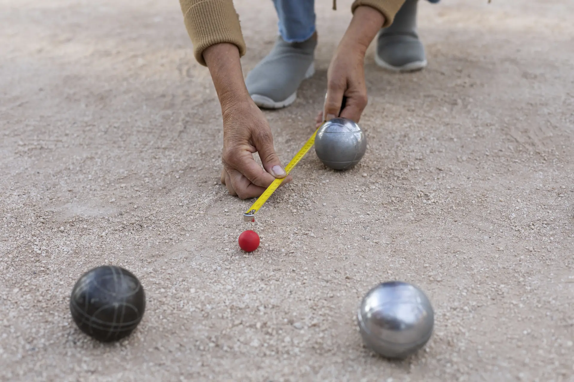 Un homme mesure la distance avec entre un cochonnet rouge et une boule de pétanque.