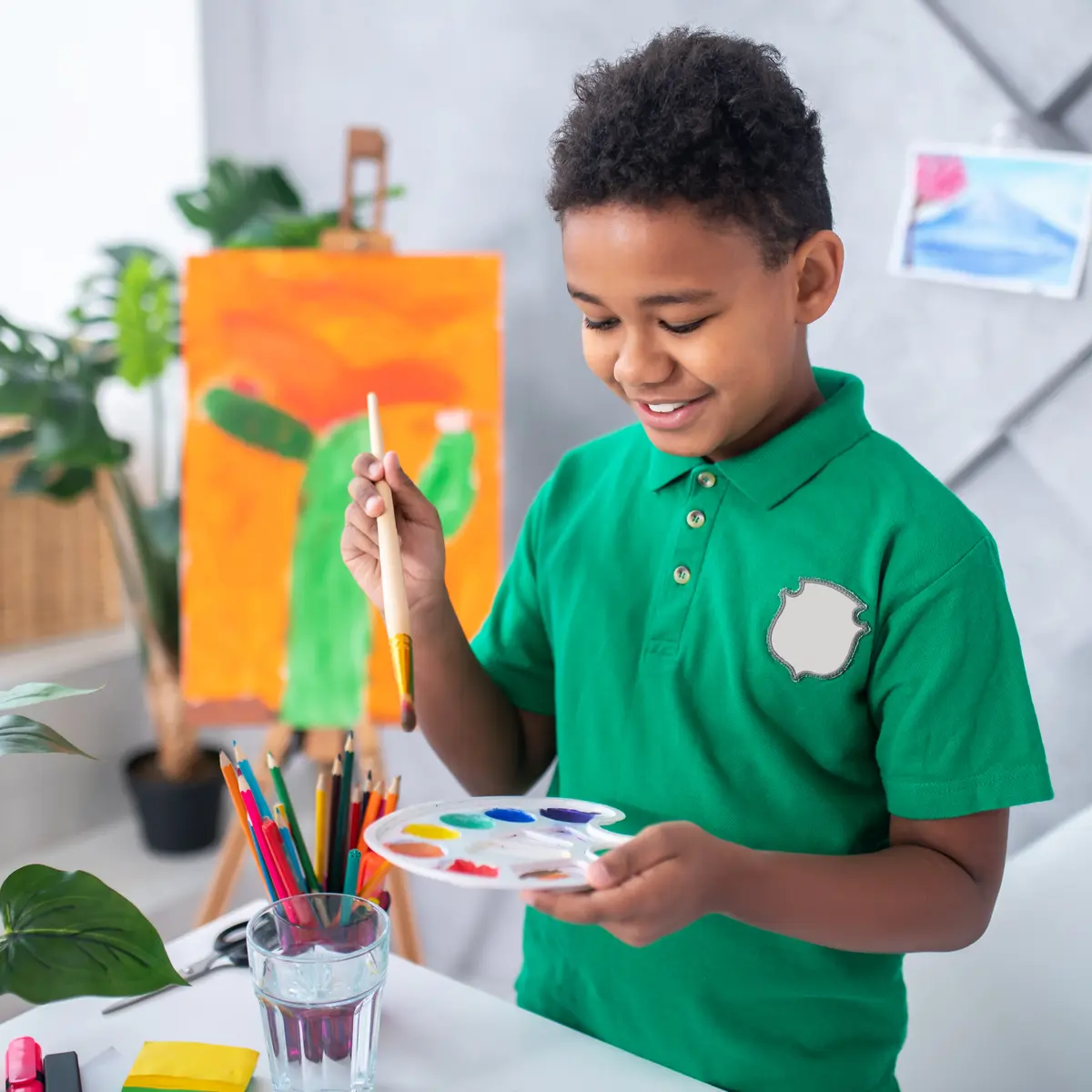 Boy looking holding paintbrush over palette with paints