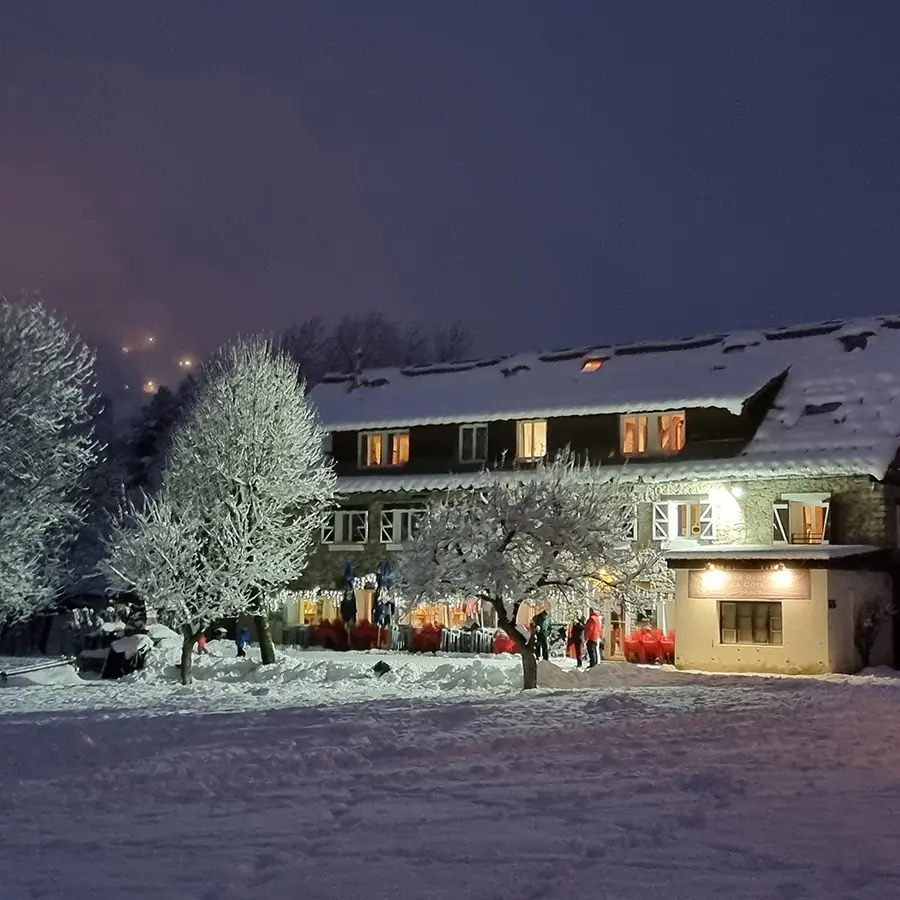 View of the restaurant in winter, a large 3-story stone building, outdoor terrace, at the back of a snowy meadow
