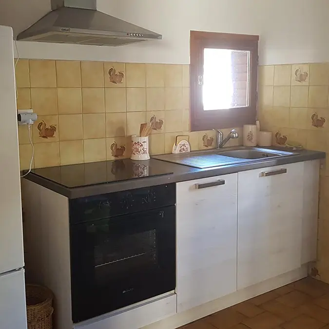 Coin cuisine carrelée avec plaques électriques, évier, fenêtres