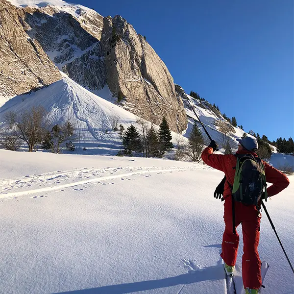 Skieur montant dans une prairie enneigée devant une falaise
